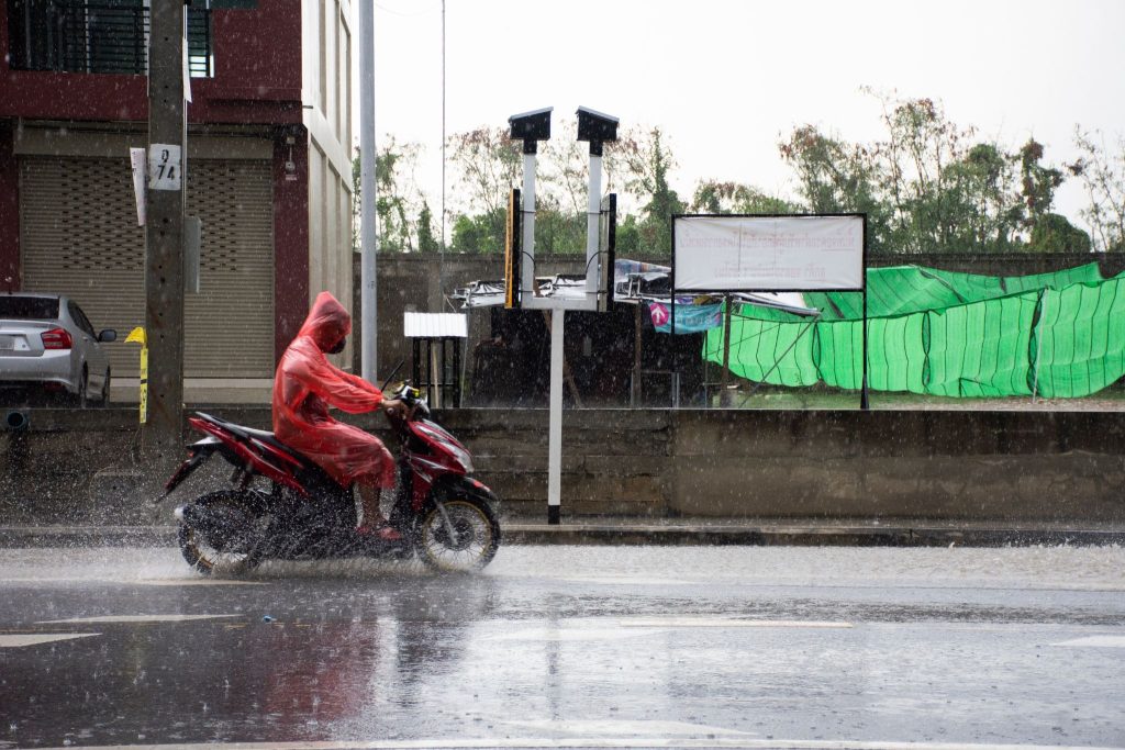 Pengendara motor memakai jas hujan merah saat hujan