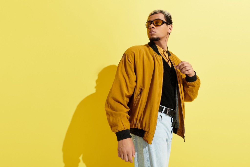 Pria memakai jaket bomber warna mustard berlatar kuning