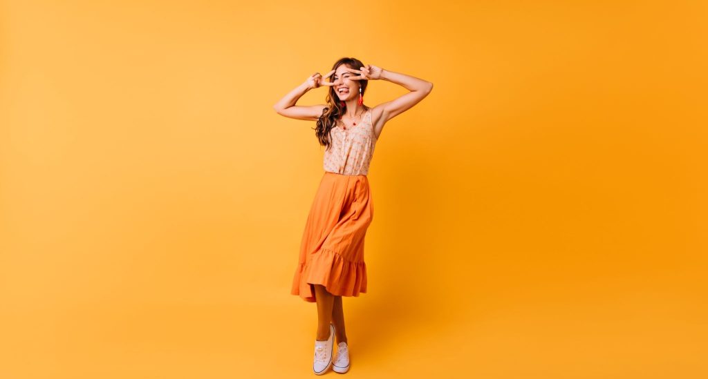 Wanita memakai rok payung oranye dan atasan putih berlatar oranye